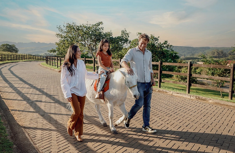 Família passeando com criança sentada no ponei branco, uma das atrações oferecidas no resort do Clara Ibiuna