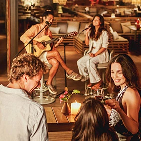 homem tocando violão enquanto mulher canta e uma família reunida curtindo o som ao vivo no resort a noite